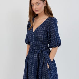 Peut inclure: Robe portefeuille bleu marine à motif quadrillé blanc. La robe présente un décolleté en V, des manches courtes bouffantes et une ceinture assortie. Elle a des poches et arrive à mi-mollet.
