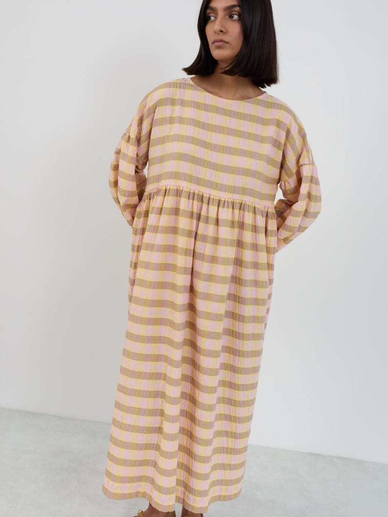 K&ouml;nnte beinhalten: Ein lang&auml;rmeliges Midikleid mit horizontalem Streifenmuster in abwechselnden Farbt&ouml;nen von Hellrosa, ged&auml;mpftem Olivgr&uuml;n und Creme. Das Kleidungsst&uuml;ck hat einen Rundhalsausschnitt, eine geraffte Taillennaht und volumin&ouml;se &Auml;rmel mit B&uuml;ndchen.