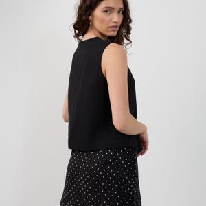 May include: A black sleeveless top and a black mini skirt with white polka dots. The top has a simple, rounded neckline. The skirt is A-line and falls above the knees. The outfit is suitable for casual or semi-formal occasions.