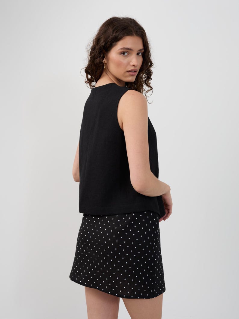 May include: A black sleeveless top and a black mini skirt with white polka dots. The top has a simple, rounded neckline. The skirt is A-line and falls above the knees. The outfit is suitable for casual or semi-formal occasions.