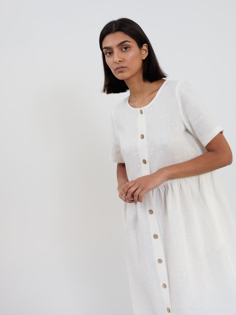 Close-up three-quarter view of the DOVE linen midi dress in Ivory showing round neckline, wooden button-front closure, and gathered waist