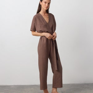 May include: A brown linen jumpsuit with a V-neckline, short sleeves, and a tie belt. The jumpsuit has a relaxed fit and is cropped at the ankle.