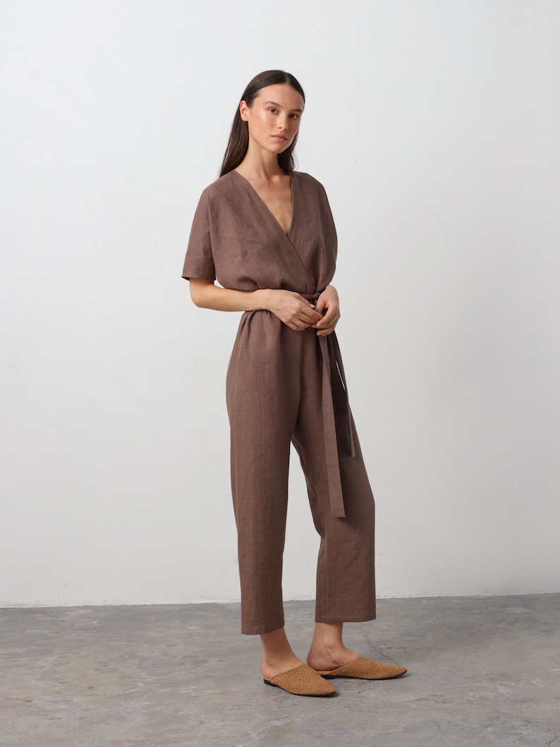 May include: A brown linen jumpsuit with a V-neckline, short sleeves, and a tie belt. The jumpsuit has a relaxed fit and is cropped at the ankle.