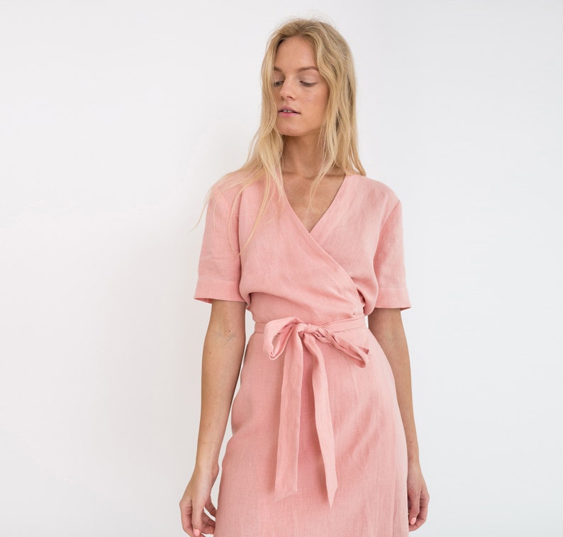 Op de afbeelding: Een roze linnen wikkeljurk met een V-hals en korte mouwen. De jurk heeft een strikceintuur in de taille.