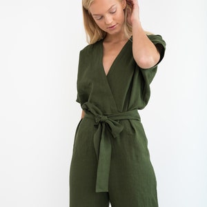 May include: A woman wearing a green linen jumpsuit with a wrap-style bodice and a self-tie belt.