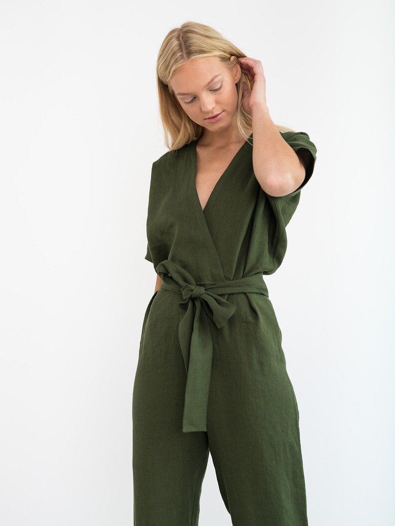 May include: A woman wearing a green linen jumpsuit with a wrap-style bodice and a self-tie belt.