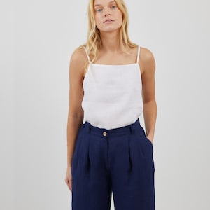 May include: A white linen tank top with thin straps and a square neckline, paired with dark blue wide-leg pants.