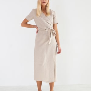 May include: A beige linen wrap dress with short sleeves and a tie belt. The dress is midi length and has a relaxed fit.