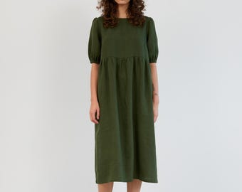 Könnte beinhalten: Ein grünes Leinen-Midikleid mit Rundhalsausschnitt und kurzen Puffärmeln. Das Kleid hat eine geraffte Taille und eine lockere Passform.