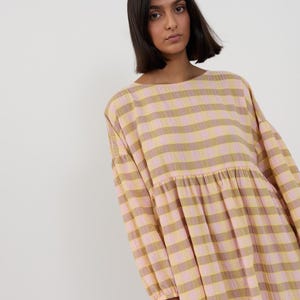K&ouml;nnte beinhalten: Ein lang&auml;rmeliges Kleid mit einem horizontalen Streifenmuster in abwechselnden T&ouml;nen von Hellrosa und ged&auml;mpftem Olivgr&uuml;n. Das Kleidungsst&uuml;ck hat einen Rundhalsausschnitt, eine geraffte Taillennaht und weite &Auml;rmel mit elastischen B&uuml;ndchen.
