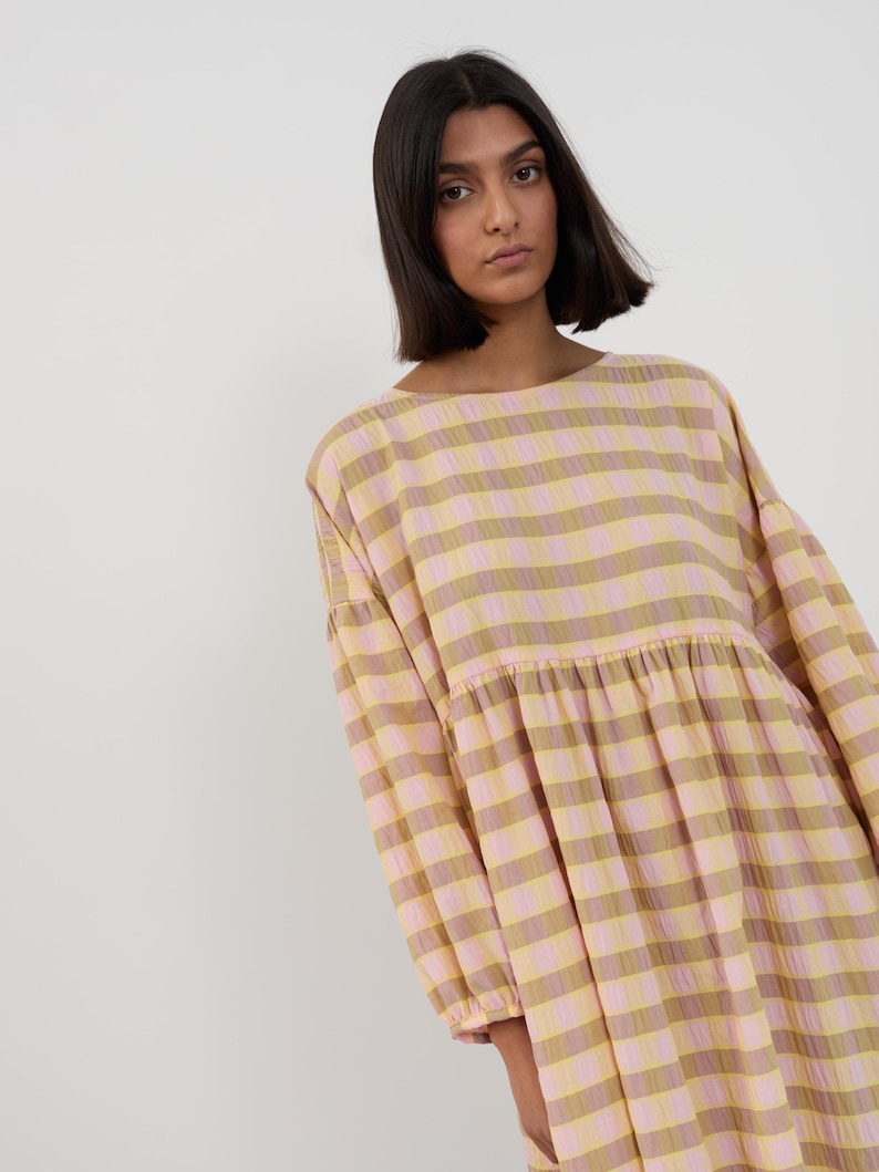 K&ouml;nnte beinhalten: Ein lang&auml;rmeliges Kleid mit einem horizontalen Streifenmuster in abwechselnden T&ouml;nen von Hellrosa und ged&auml;mpftem Olivgr&uuml;n. Das Kleidungsst&uuml;ck hat einen Rundhalsausschnitt, eine geraffte Taillennaht und weite &Auml;rmel mit elastischen B&uuml;ndchen.