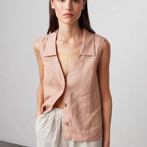 Pu&ograve; includere: Un top in lino senza maniche con un colletto e una chiusura con bottoni. Il top &egrave; di colore rosa chiaro e viene indossato sopra pantaloni in lino a righe.