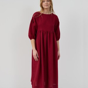May include: A burgundy midi dress with a round neckline and 3/4 sleeves. The dress has a gathered waist and a slightly flared skirt.
