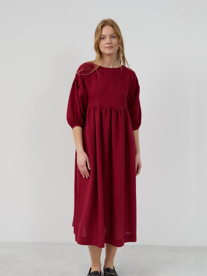 May include: A burgundy midi dress with a round neckline and 3/4 sleeves. The dress has a gathered waist and a slightly flared skirt.
