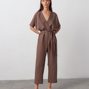May include: A brown linen jumpsuit with a wrap-style bodice and a tie belt. The jumpsuit has short sleeves and a V-neckline.