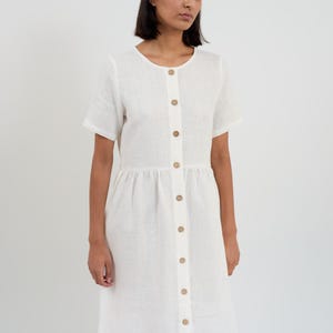 Front three-quarter view of the DOVE dress in Ivory showing the short sleeves, round neckline, and wooden buttons with gathered skirt