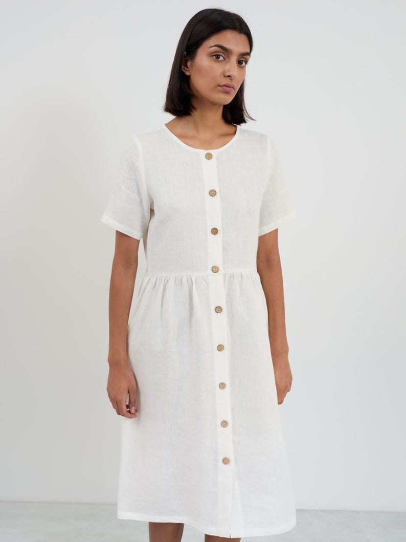 Front three-quarter view of the DOVE dress in Ivory showing the short sleeves, round neckline, and wooden buttons with gathered skirt