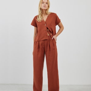 May include: A rust-colored linen top with a V-neck and short sleeves, paired with matching rust-colored linen pants. The top has a button-up front and a relaxed fit.