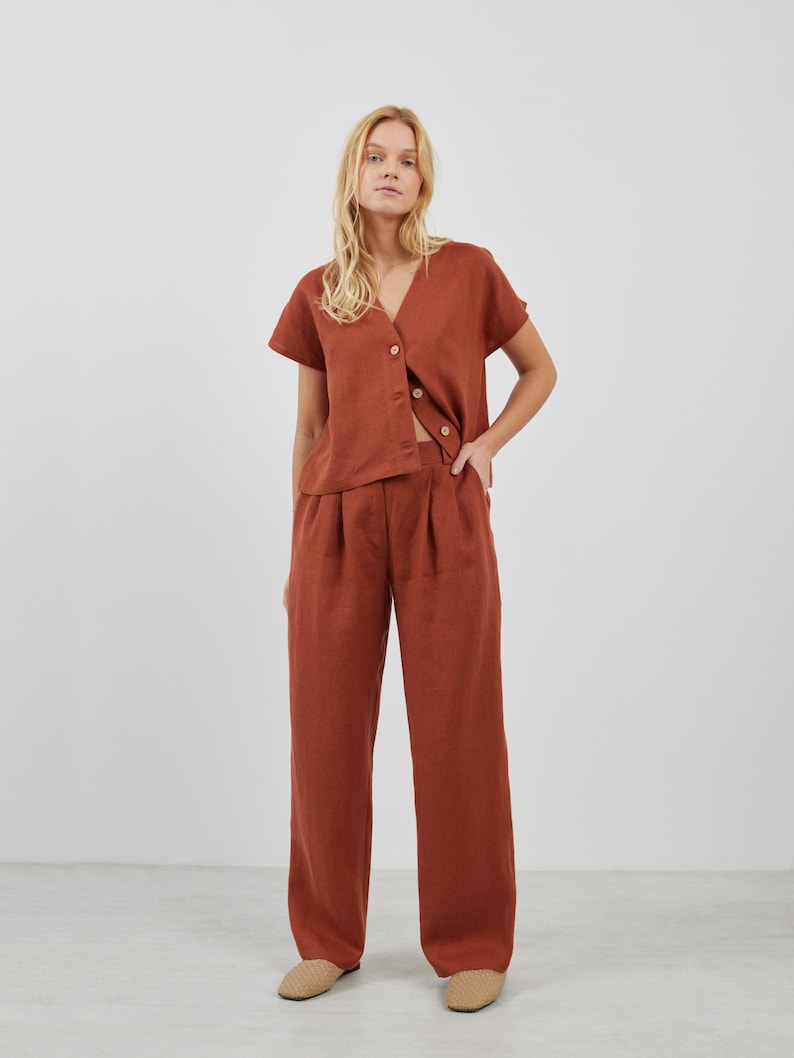 May include: A rust-colored linen top with a V-neck and short sleeves, paired with matching rust-colored linen pants. The top has a button-up front and a relaxed fit.