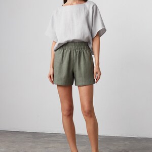 Pode incluir: Uma mulher est&aacute; vestindo uma blusa de linho cinza claro e shorts de linho verde oliva com c&oacute;s el&aacute;stico. Ela est&aacute; usando sapatos pretos de couro tran&ccedil;ado.