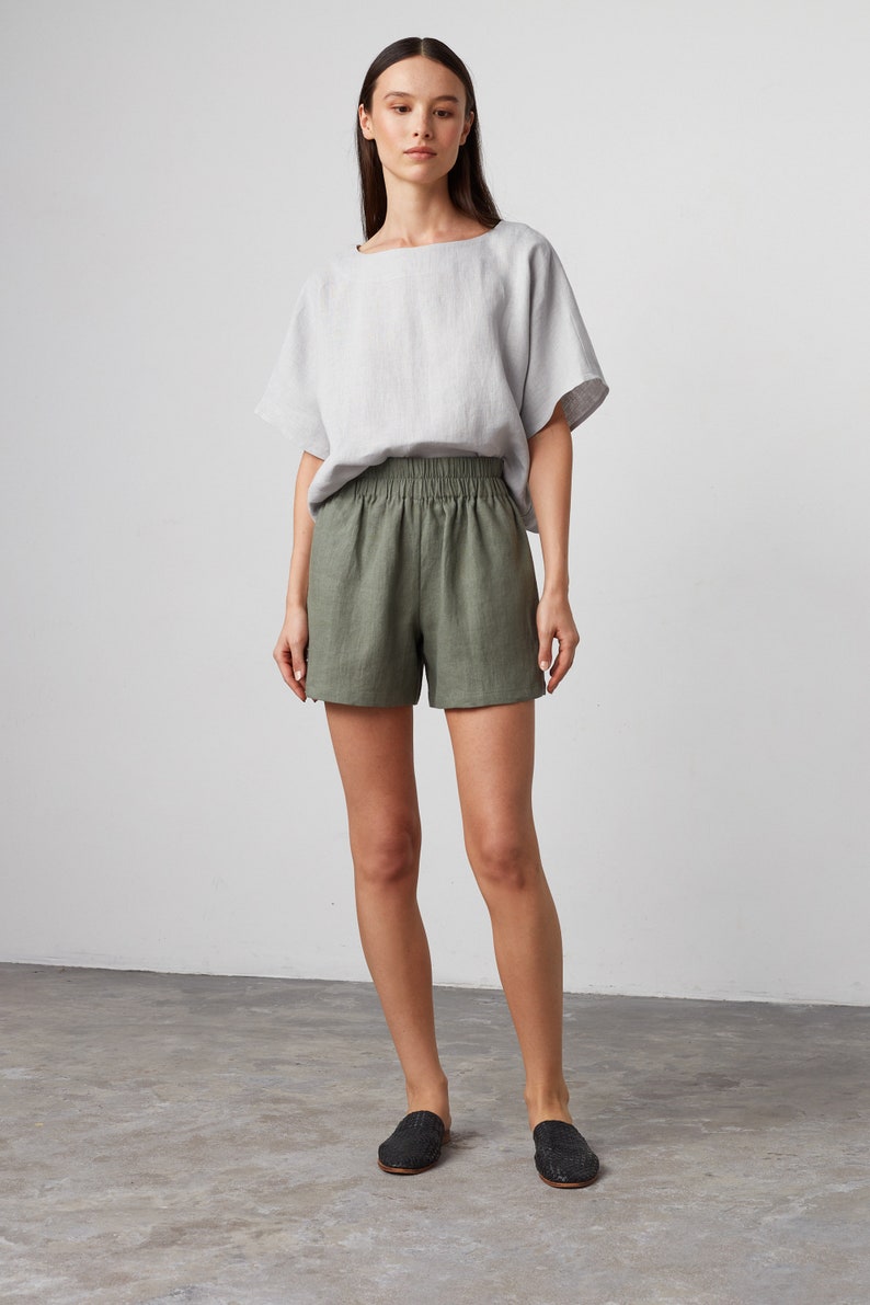 Pode incluir: Uma mulher est&aacute; vestindo uma blusa de linho cinza claro e shorts de linho verde oliva com c&oacute;s el&aacute;stico. Ela est&aacute; usando sapatos pretos de couro tran&ccedil;ado.