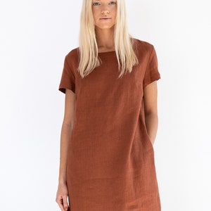 May include: A rust-colored linen dress with short sleeves and a square neckline. The dress has a relaxed fit and a slightly A-line silhouette.