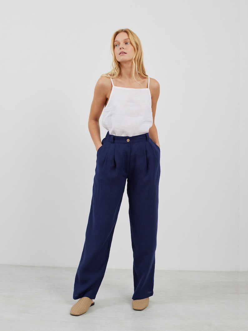 May include: A woman is wearing a white linen tank top and dark blue wide-leg linen pants. She is wearing tan leather sandals.