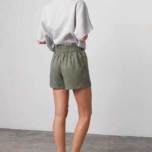 Pode incluir: Uma mulher vestindo uma blusa de linho cinza claro e shorts de linho verde oliva com c&oacute;s el&aacute;stico. Ela est&aacute; usando mules de couro preto.