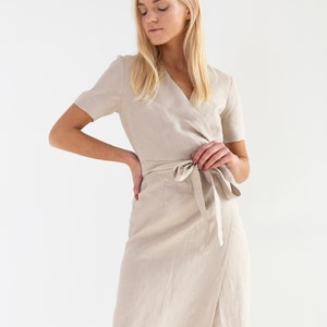 May include: A beige linen wrap dress with short sleeves and a tie at the waist.