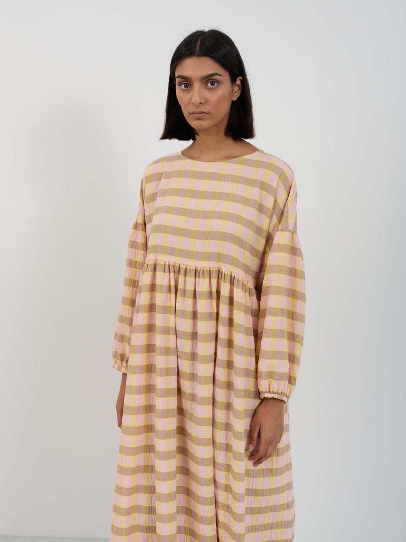 K&ouml;nnte beinhalten: Ein lang&auml;rmeliges Midikleid mit einem horizontalen Streifenmuster in abwechselnden Farbt&ouml;nen von Hellrosa und ged&auml;mpftem Olivgr&uuml;n. Das Kleidungsst&uuml;ck hat einen Rundhalsausschnitt, eine geraffte Taille und weite &Auml;rmel mit elastischen B&uuml;ndchen.