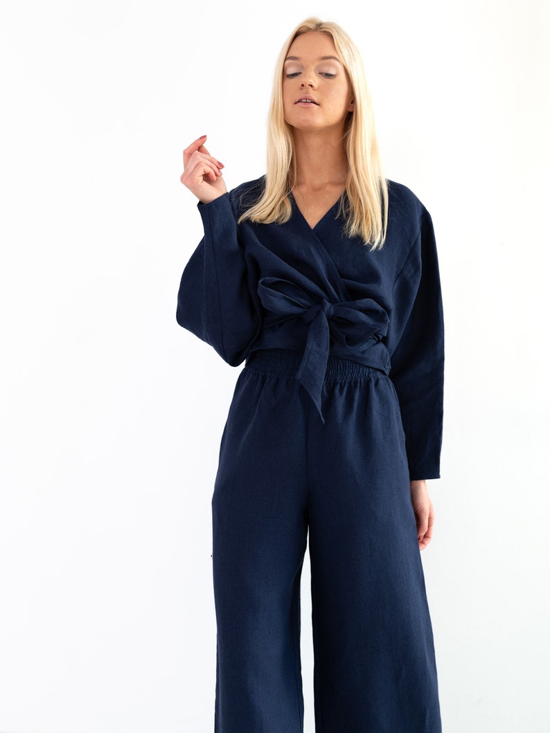 May include: A navy blue linen wrap top and wide-leg pants set. The top has a V-neckline and ties at the waist. The pants have a relaxed fit and a drawstring waist.