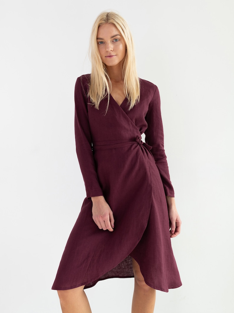 Pu&ograve; includere: Un abito avvolgente color bordeaux con maniche lunghe e cintura a nodo. L'abito ha una scollatura a V e una lunghezza midi.