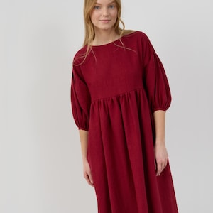 May include: A burgundy midi dress with a round neckline and puffed sleeves. The dress has a gathered waist and a relaxed fit.