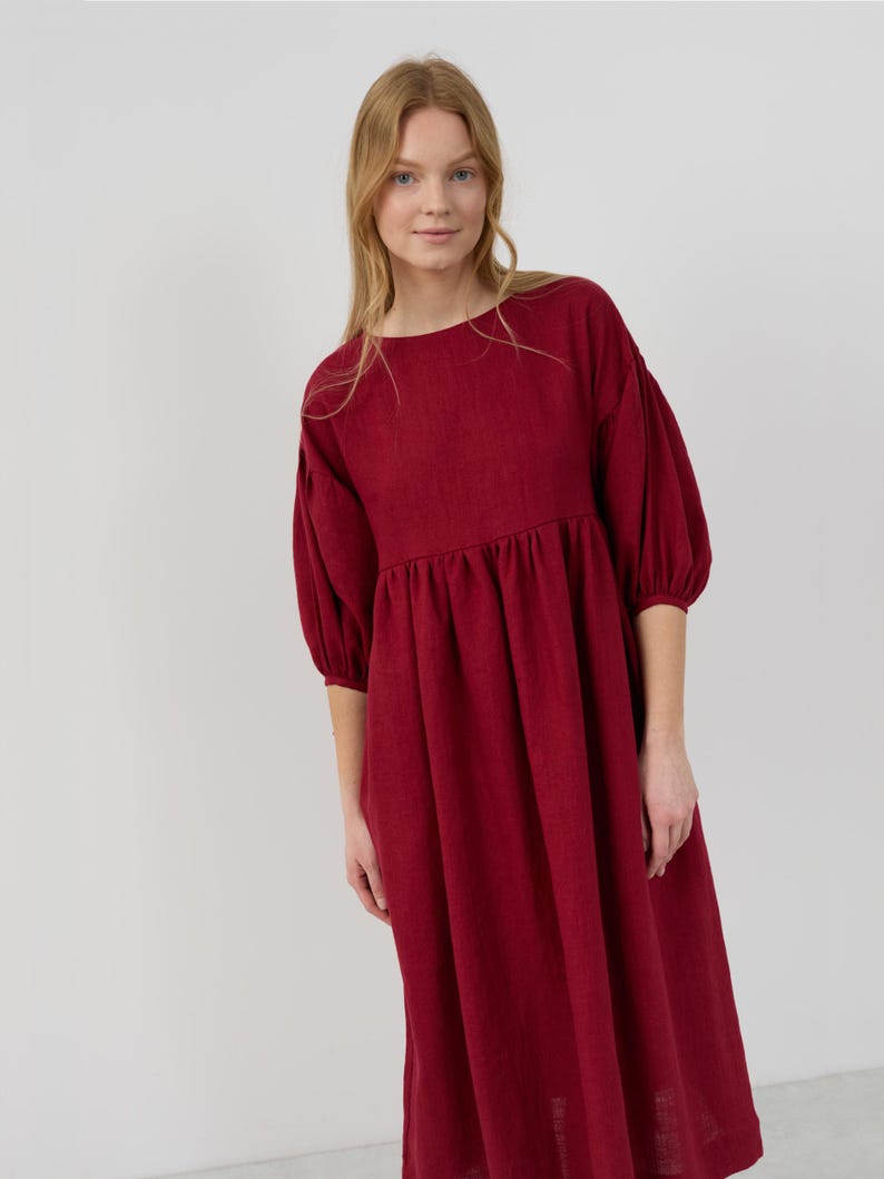 May include: A burgundy midi dress with a round neckline and puffed sleeves. The dress has a gathered waist and a relaxed fit.