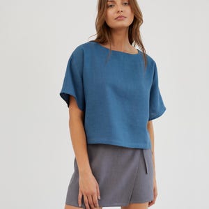 Puede incluir: Una mujer lleva una blusa de lino azul con mangas cortas y una falda de lino gris envolvente.