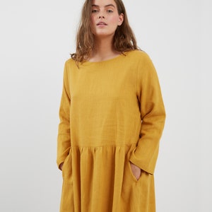 May include: A long-sleeved, yellow linen dress with a round neckline and pockets. The dress has a gathered waist and a flowing skirt.