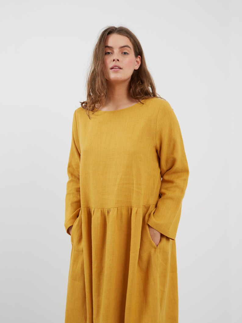 May include: A long-sleeved, yellow linen dress with a round neckline and pockets. The dress has a gathered waist and a flowing skirt.