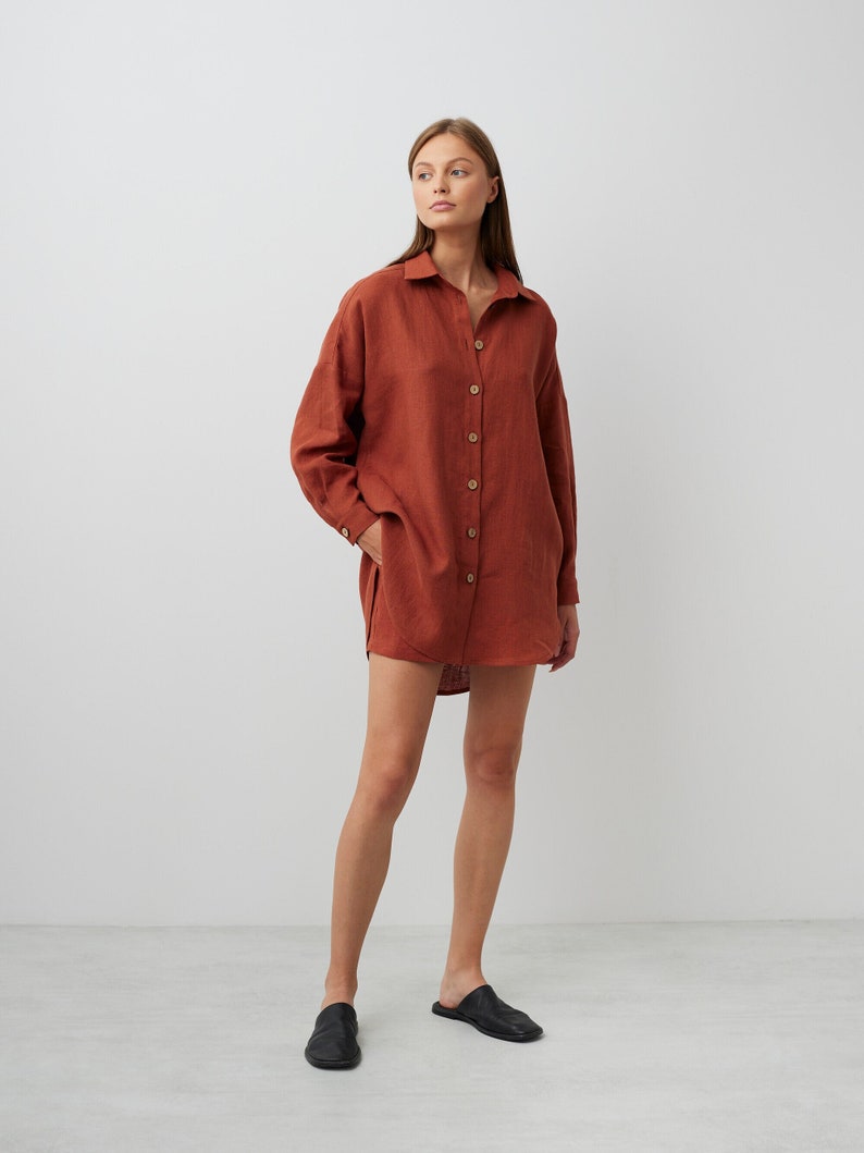 May include: A rust-colored linen shirt dress with a collared neckline and button closure. The dress has long sleeves and a relaxed fit.