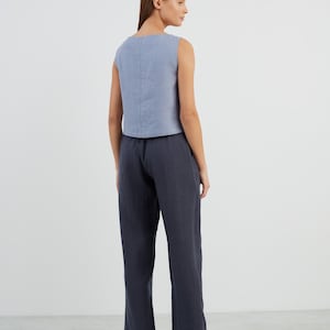 May include: A woman is wearing a light blue sleeveless linen top and dark blue linen trousers. She is wearing black loafers.