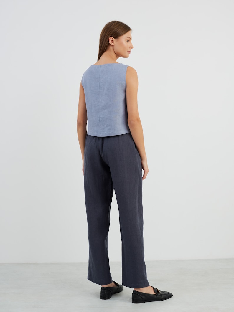May include: A woman is wearing a light blue sleeveless linen top and dark blue linen trousers. She is wearing black loafers.