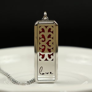 Op de afbeelding: Zilveren ketting met hanger met een rood filigraanontwerp en het woord "love" gegraveerd op de voorkant.