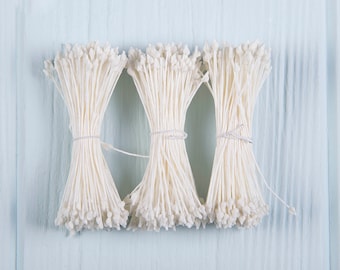 May include: Three bundles of white flower stamens, tied together with white string, on a light blue wooden surface.
