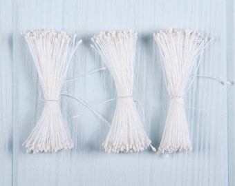 May include: Three bundles of white floral stems, tied together with string, on a light blue wooden background.