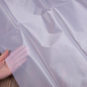 Könnte beinhalten: Ein weißes, durchscheinendes, stoffartiges Material mit glatter Textur. Das Material ist gefaltet und wird von einer Hand gehalten.