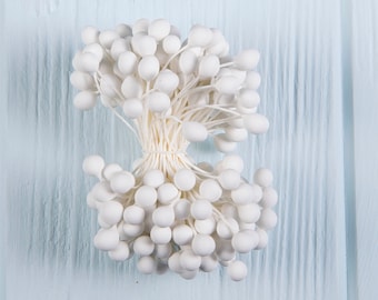 May include: A bunch of white flower buds with long stems, tied together at the base. The buds are arranged in a circular shape, with the stems radiating outwards.
