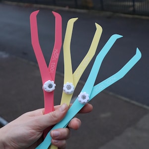 Puede incluir: Una mano sostiene cuatro herramientas de medición Kool Tool de colores. Las herramientas son rosa, amarillo y azul, cada una con una perilla de ajuste blanca en forma de engranaje. El texto "Kool Tool" está impreso en cada herramienta.