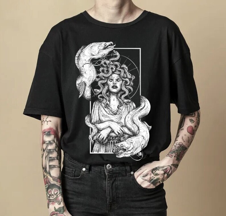 Op de afbeelding: Zwart T-shirt met een witte grafische print van Medusa, een mythische Griekse figuur met slangenhaar, omringd door paling.