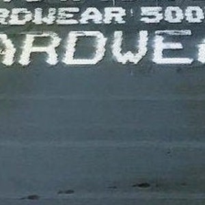 Puede incluir: Primer plano de una superficie met&aacute;lica gris con texto pintado en blanco que dice "HARDWEAR 500F MT HARDWEAR 5".