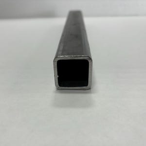 May include: A close-up of a rectangular, hollow metal tube. The tube is silver in color and has a square opening. The tube is made of a durable material and is likely used for construction or industrial purposes.