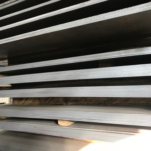May include: A stack of gray metal sheets, likely steel, are stacked on top of each other. The sheets are arranged in a neat and organized manner, with each sheet slightly offset from the one below it. The sheets are all the same size and shape, and they appear to be new and unused.